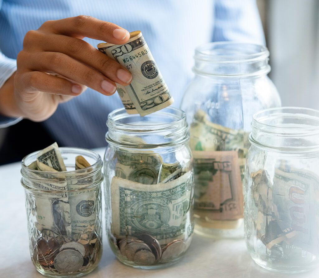 A hand putting a dollar bill in a jar