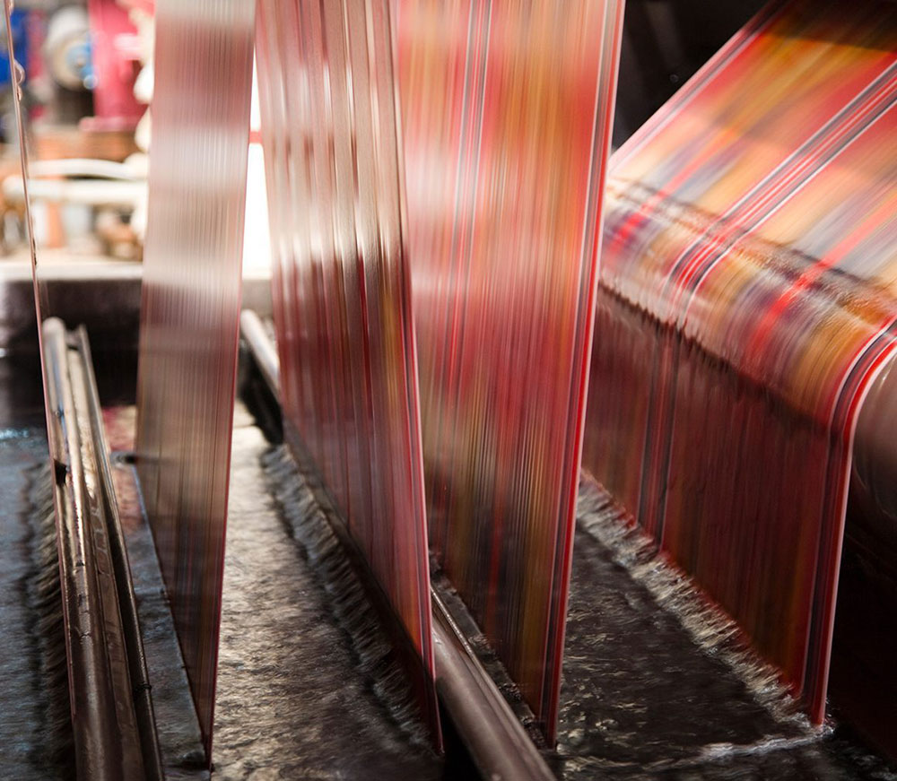 Textile manufacturing process showing dyed fabric moving through a water bath, illustrating wastewater generation during fabric dyeing and finishing.