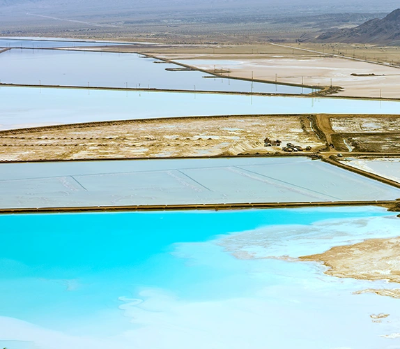 Evaporation ponds used for lithium extraction, showing shallow rectangular pools of blue and white brine in an arid landscape.