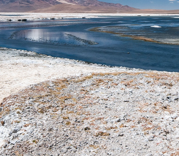 Saline water channels flowing through a mineral extraction site, with white mineral deposits and distant mountains in a dry environment.